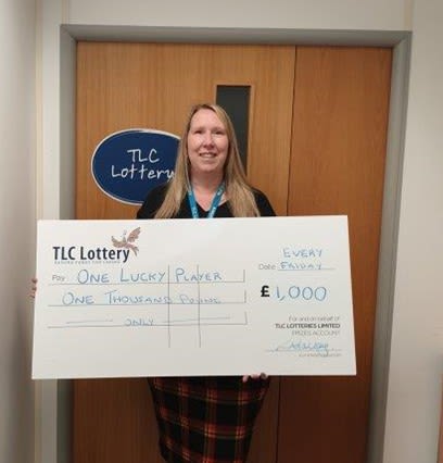 Image shows a lady holding a cheque, smiling 